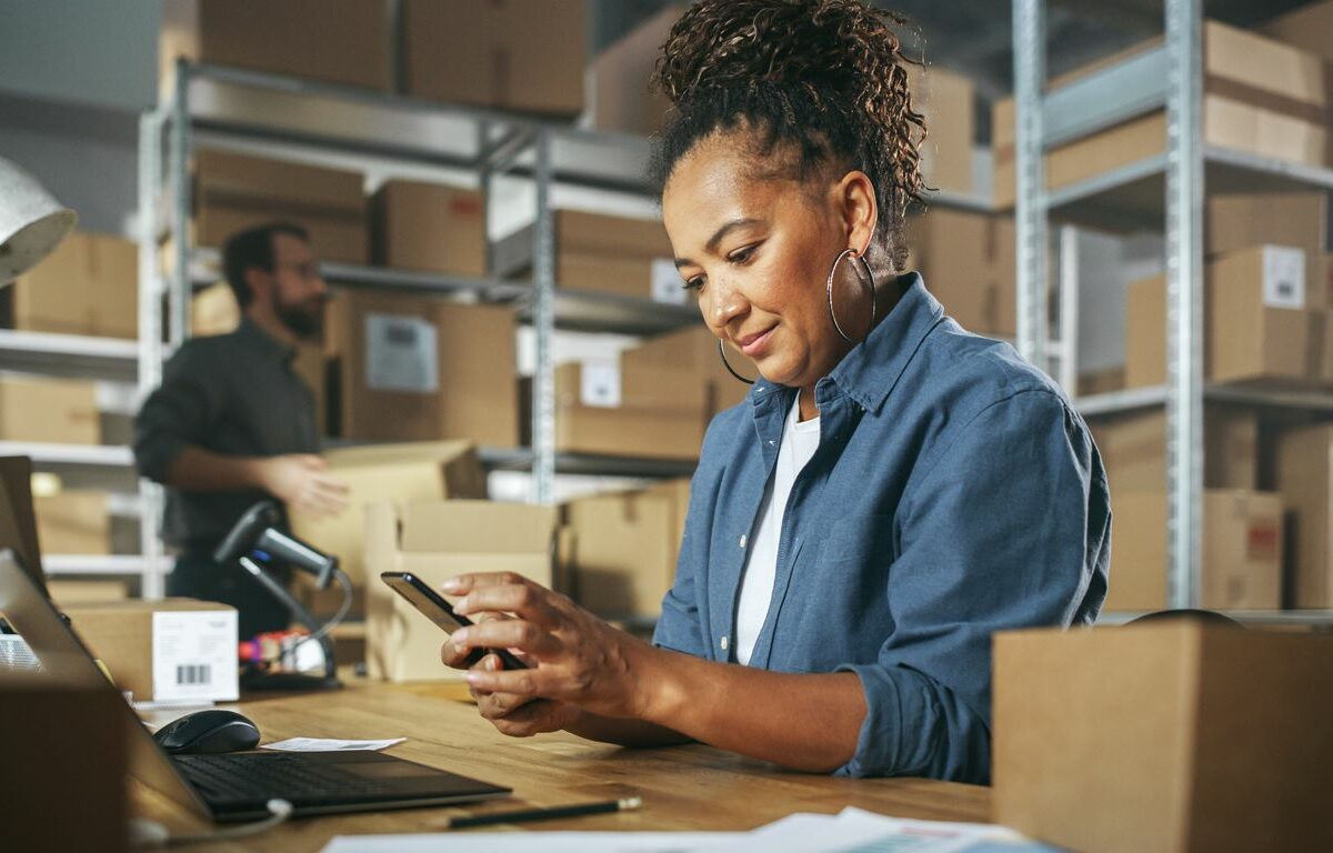 A woman and man work in a small business office cluttered with boxes.