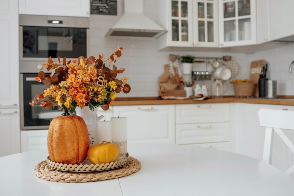 A centerpiece of pumpkins and autumnal flowers sits on a pristine, white kitchen table. 