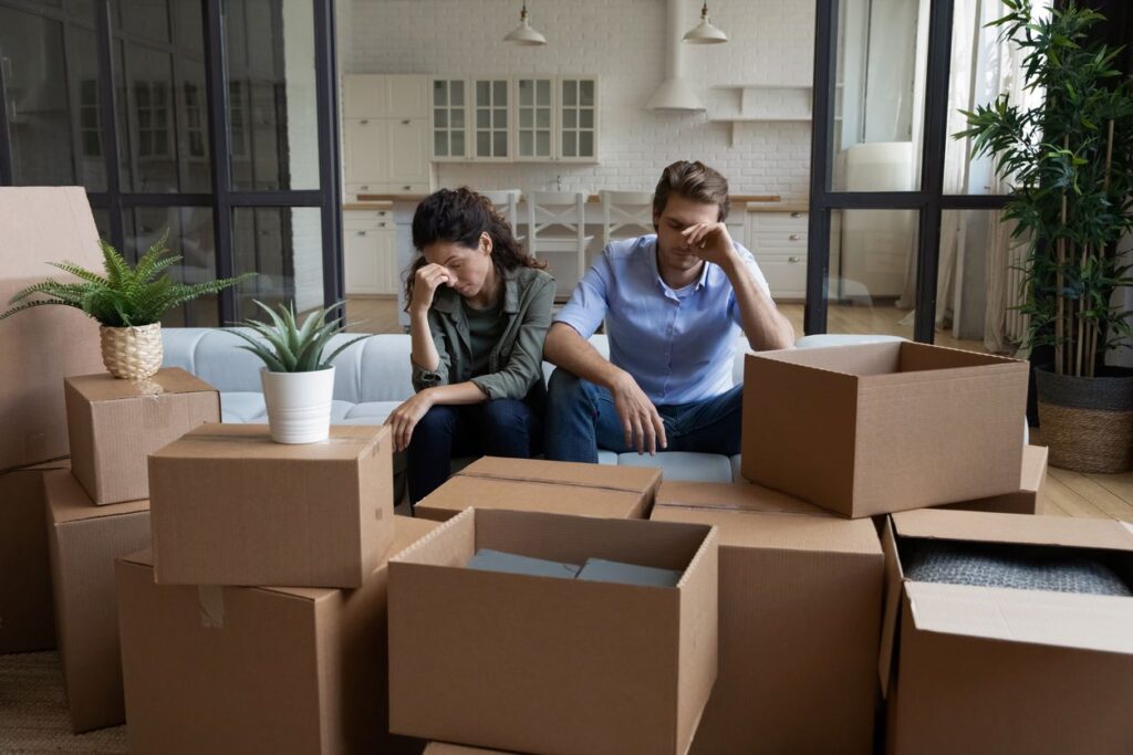 An unhappy couple surrounded by boxes of items ready for storage.