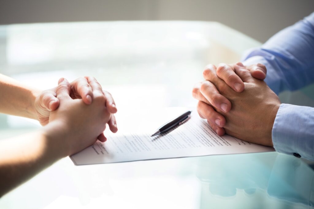 Two people sitting at a table with a piece of paper and pen in between them.