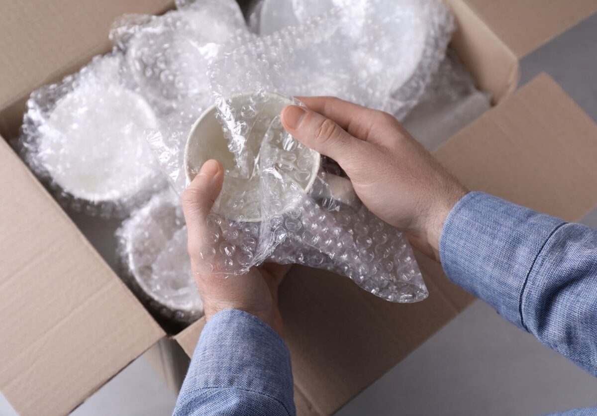 A man packs coffee mugs delicately into a cardboard box.