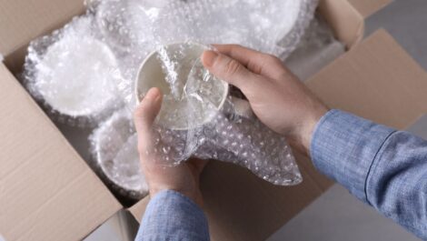 A man packs coffee mugs delicately into a cardboard box.