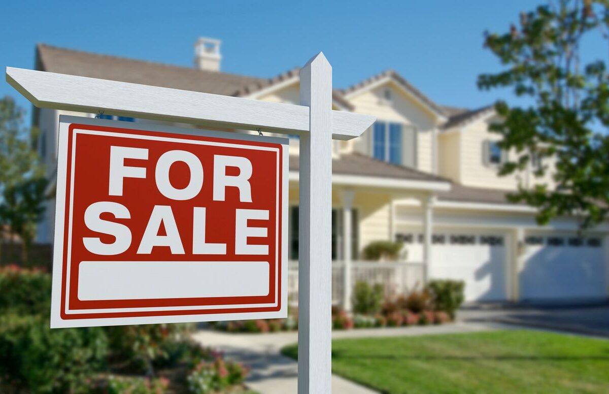 A home with a for sale sign surrounded by spring trees.