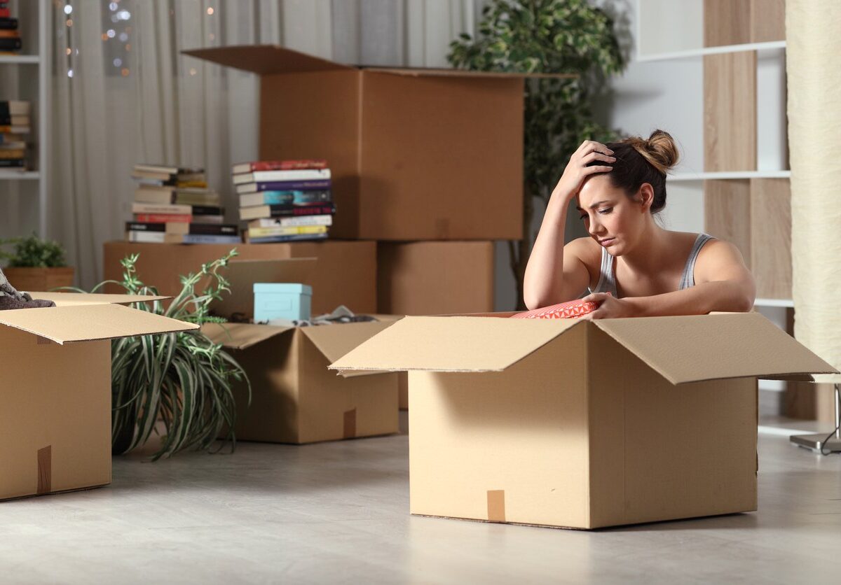 A frustrated woman looking into a moving box with several other boxes stacked behind her.