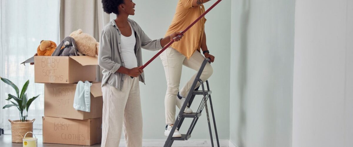 A happy couple smiles as they repaint a bedroom during a home renovation.