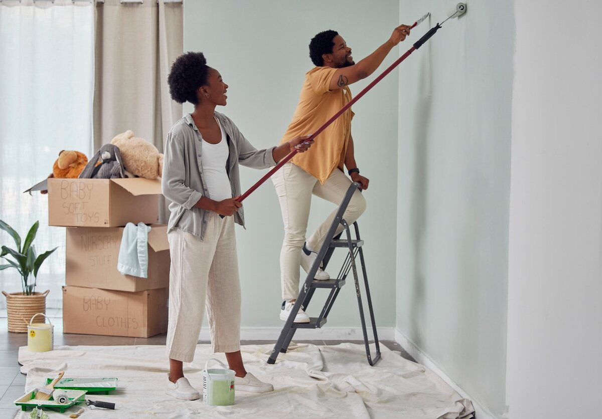 A happy couple smiles as they repaint a bedroom during a home renovation.