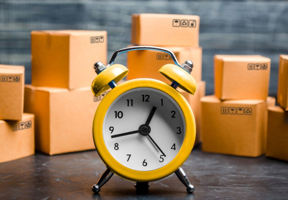 A yellow clock sitting in front of several stacks of moving boxes.